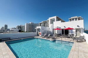 A rooftop swimming pool with lounge chairs and umbrellas, surrounded by modern buildings. - South Beach Apt with Rooftop Pool & Bay Views #304 (Miami Beach)