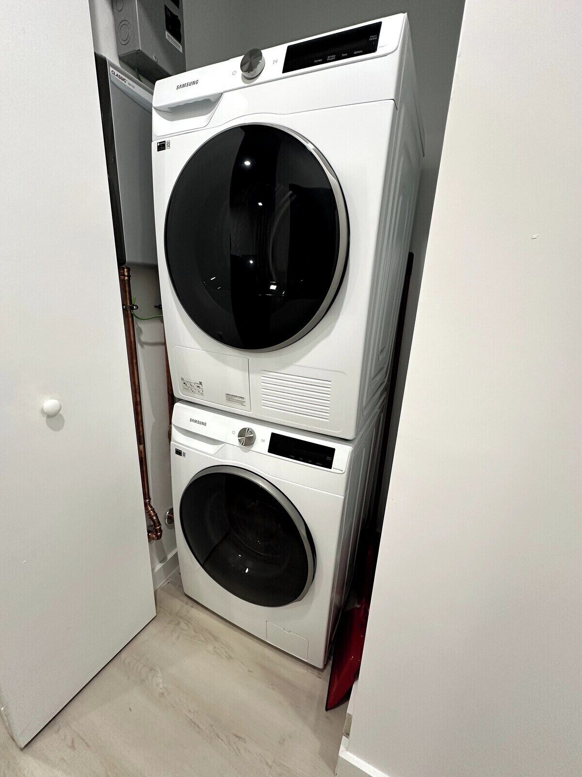 Eine kompakte, weiße, übereinander gestellte Waschmaschine und Trockner in einem schmalen Raum.