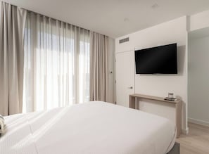 A hotel room with a bed, a TV mounted on the wall, a bedside table, and a window with curtains. - South Beach Apt with Rooftop Pool & Bay Views #304 (Miami Beach)