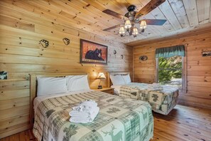 Une chambre de style cabane avec deux lits, des murs en bois, un ventilateur de plafond et une affiche accrochée au mur.