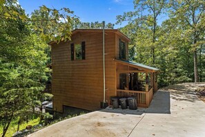 Une cabane en bois avec un porche, entourée d’arbres.
