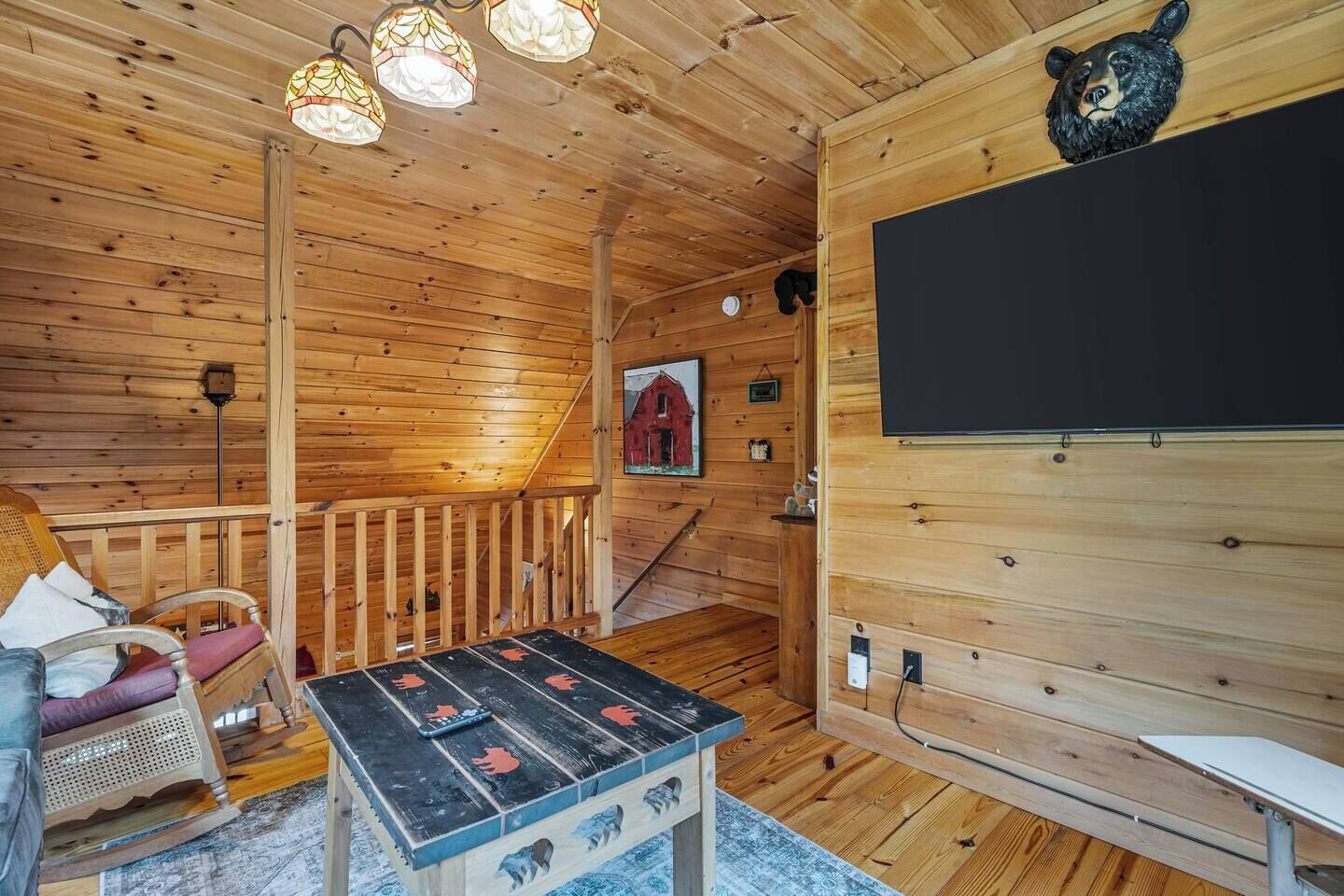 A wooden cabin interior with a wooden staircase, a table with a bear design, a bear head decoration, and a blackboard.