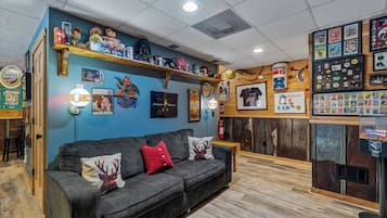 Una habitación con un sofá gris oscuro, estantes de madera con diversos objetos, y una pared decorada con cuadros y recuerdos.