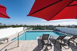 A rooftop pool with clear blue water, surrounded by lounge chairs and umbrellas, overlooking a cityscape. - South Beach Apt: Rooftop Pool/Prime Location #201 (Miami Beach)