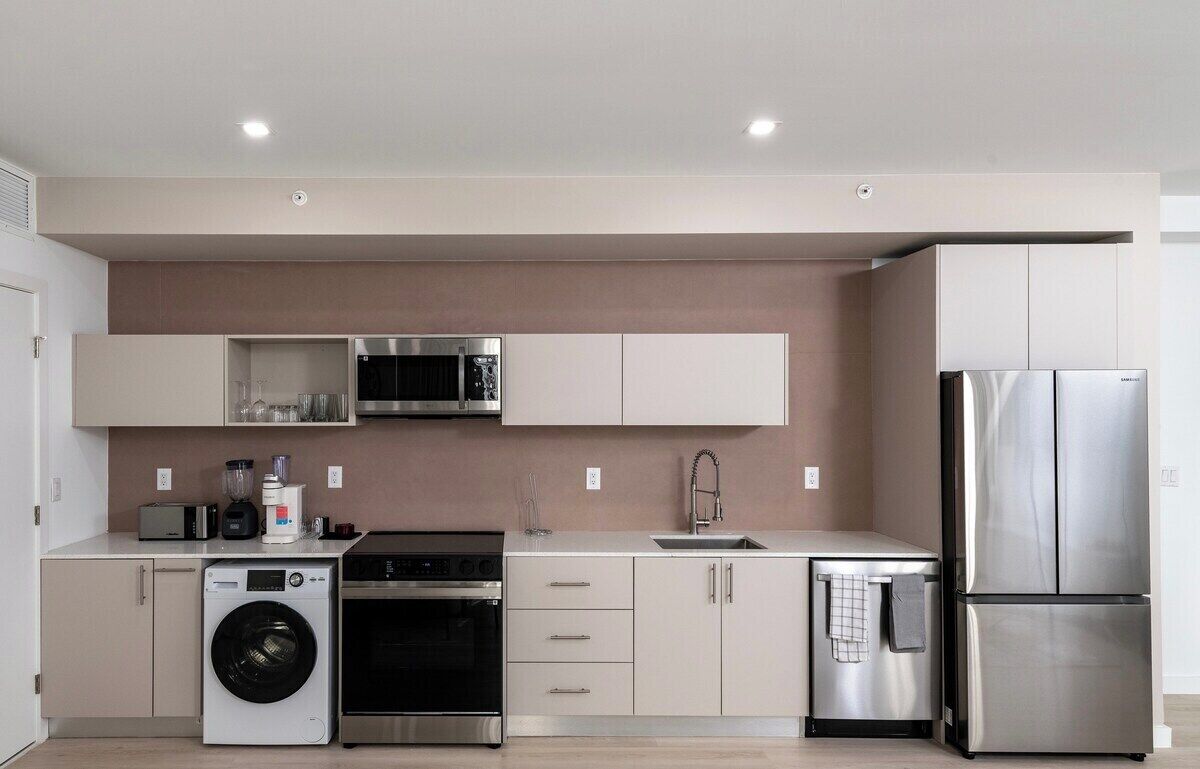 Eine moderne Küche mit Edelstahlgeräten, darunter eine Waschmaschine, ein Backofen, eine Mikrowelle und ein Kühlschrank.
