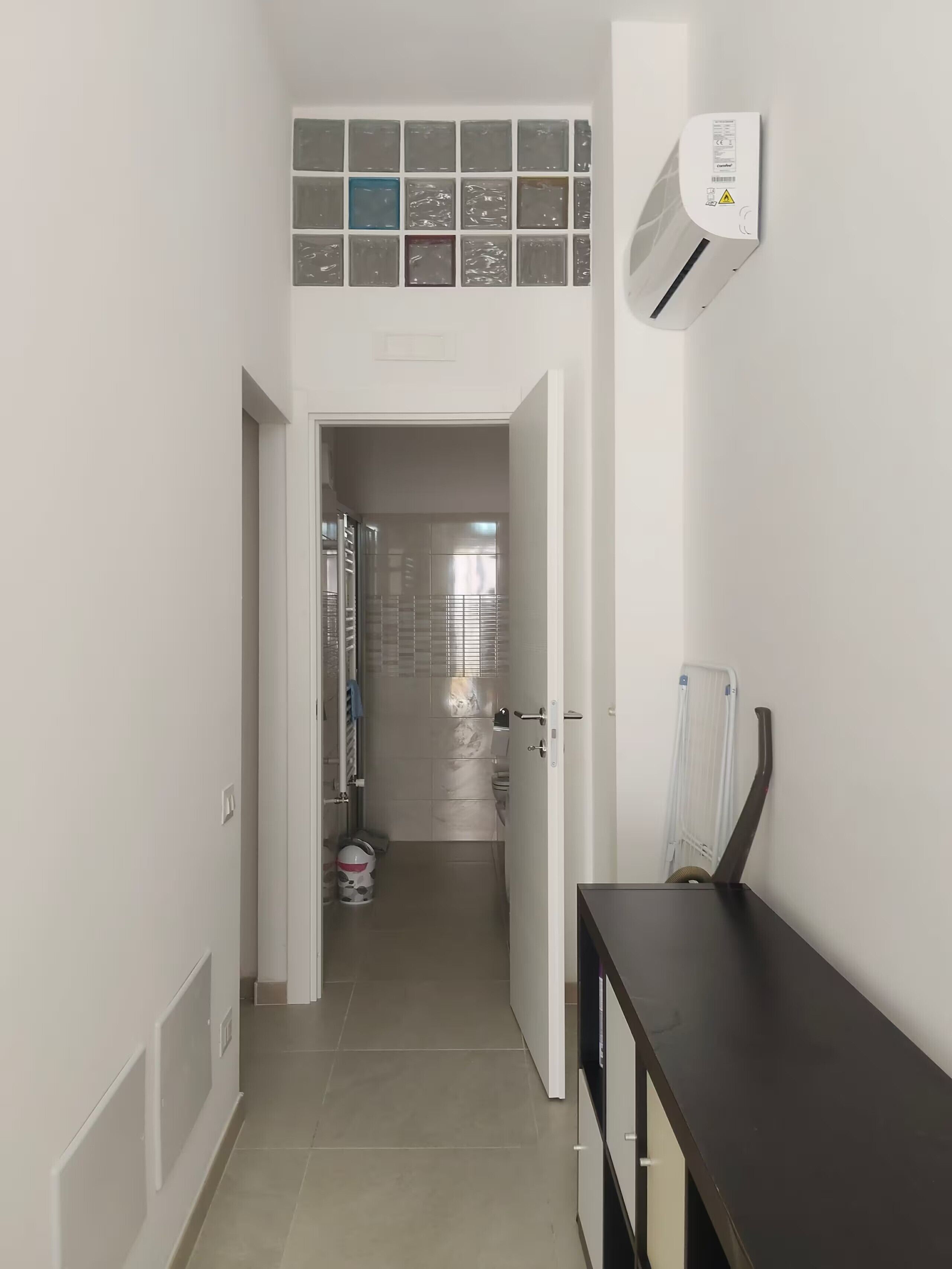 Un couloir menant à une salle de bain équipée de toilettes, d’une douche et d’un porte-serviettes.