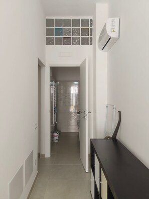 A hallway leading to a bathroom with a toilet, a shower, and a towel rack.