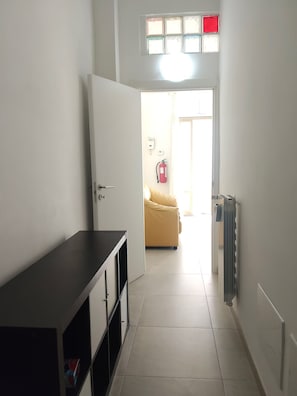 A hallway with a door leading to a room, a radiator, and a fire extinguisher on the wall.