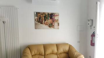 Ein Zimmer mit einem beigen Sofa, einem Heizkörper, einem Wandbild und einem Feuerlöscher.