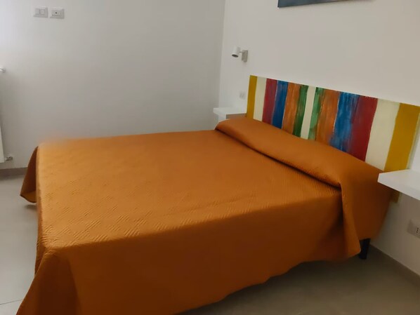 A single bed with an orange bedspread in a room with white walls and a colorful striped headboard.