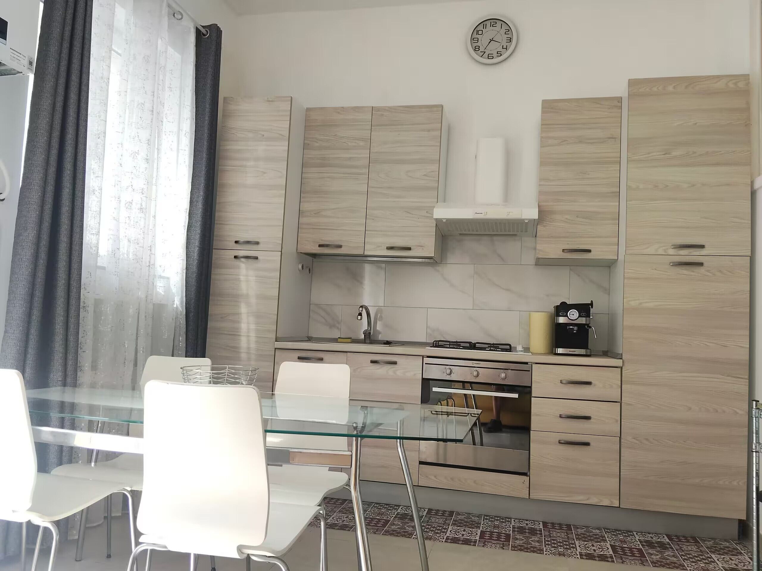 Eine moderne Küche mit einem Glastisch, weißen Stühlen, einer Kaffeemaschine und einer Uhr an der Wand.