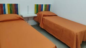 Ein Zimmer mit zwei Betten, jedes mit einer orangefarbenen Decke, einem weißen Nachttisch und einer farbenfrohen Wanddekoration mit Streifen.