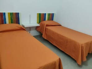 Ein Zimmer mit zwei Betten, jedes mit einer orangefarbenen Decke, einem weißen Nachttisch und einer farbenfrohen Wanddekoration mit Streifen.