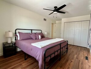 A bedroom with a bed, nightstands, a ceiling fan, and a wardrobe.
