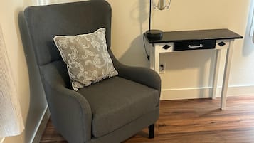 A grey armchair with a patterned pillow, a black desk with drawers, and a wall-mounted lamp.