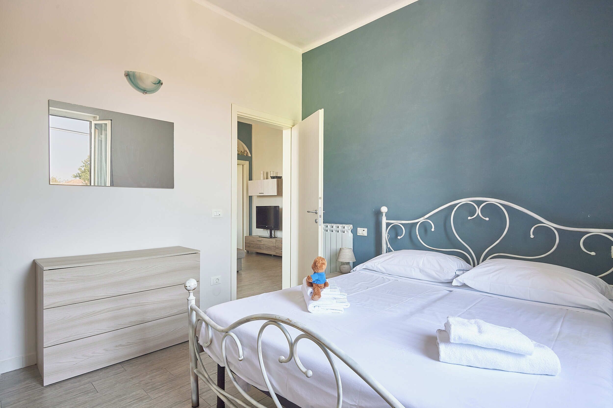 A bedroom with a bed, a dresser, a mirror, and a television in the adjacent room.