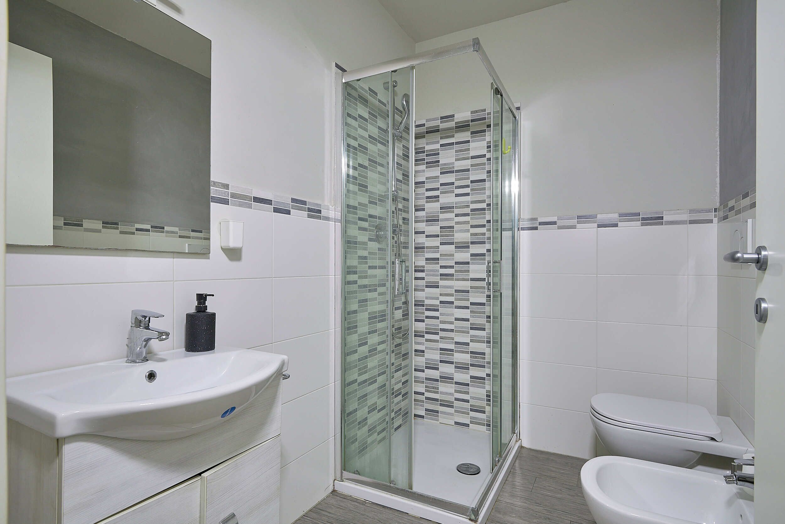 Un bagno con doccia vetro-murata, un lavandino con dispenser di sapone e un water.