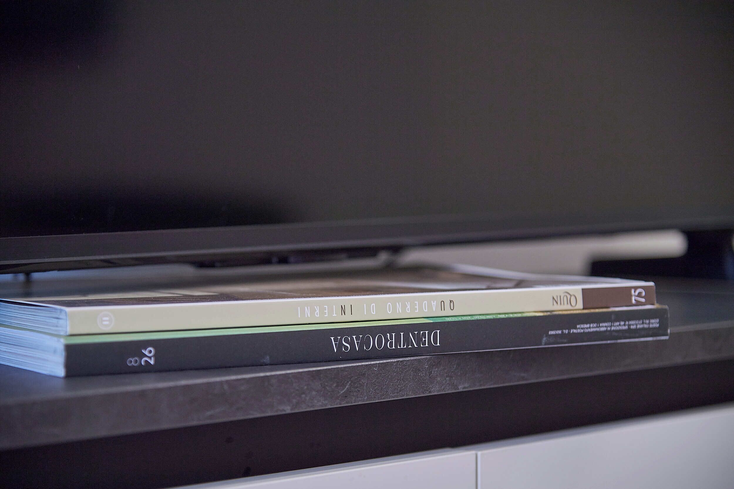Un televisor de pantalla plana montado en la pared, con un estante debajo que sostiene una pila de libros.