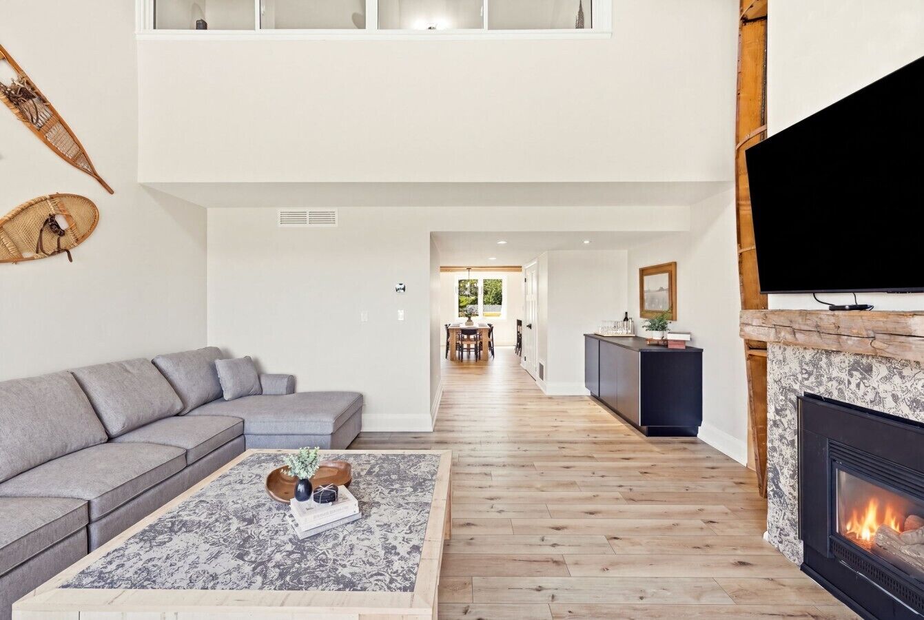 A modern living room with a grey sofa, a coffee table with decorative items, a fireplace, and a television mounted on the wall.
