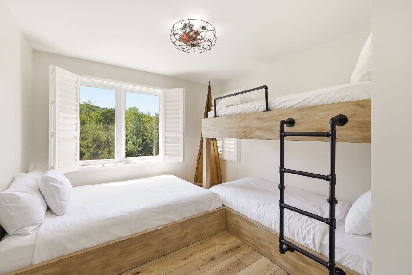 A bedroom with a bunk bed, a window with shutters, and a wooden floor.