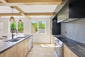 A modern kitchen with a large island, built-in oven, and a view of the outdoors through large windows. - Renovated Alpine Retreat | Ski & Golf Views (The Blue Mountains)