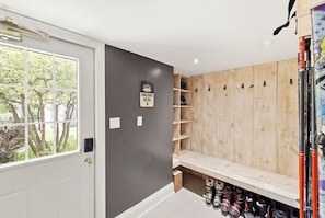 A room with a white door, a grey wall, and a wooden bench with shoe storage underneath. - Renovated Alpine Retreat | Ski & Golf Views (The Blue Mountains)