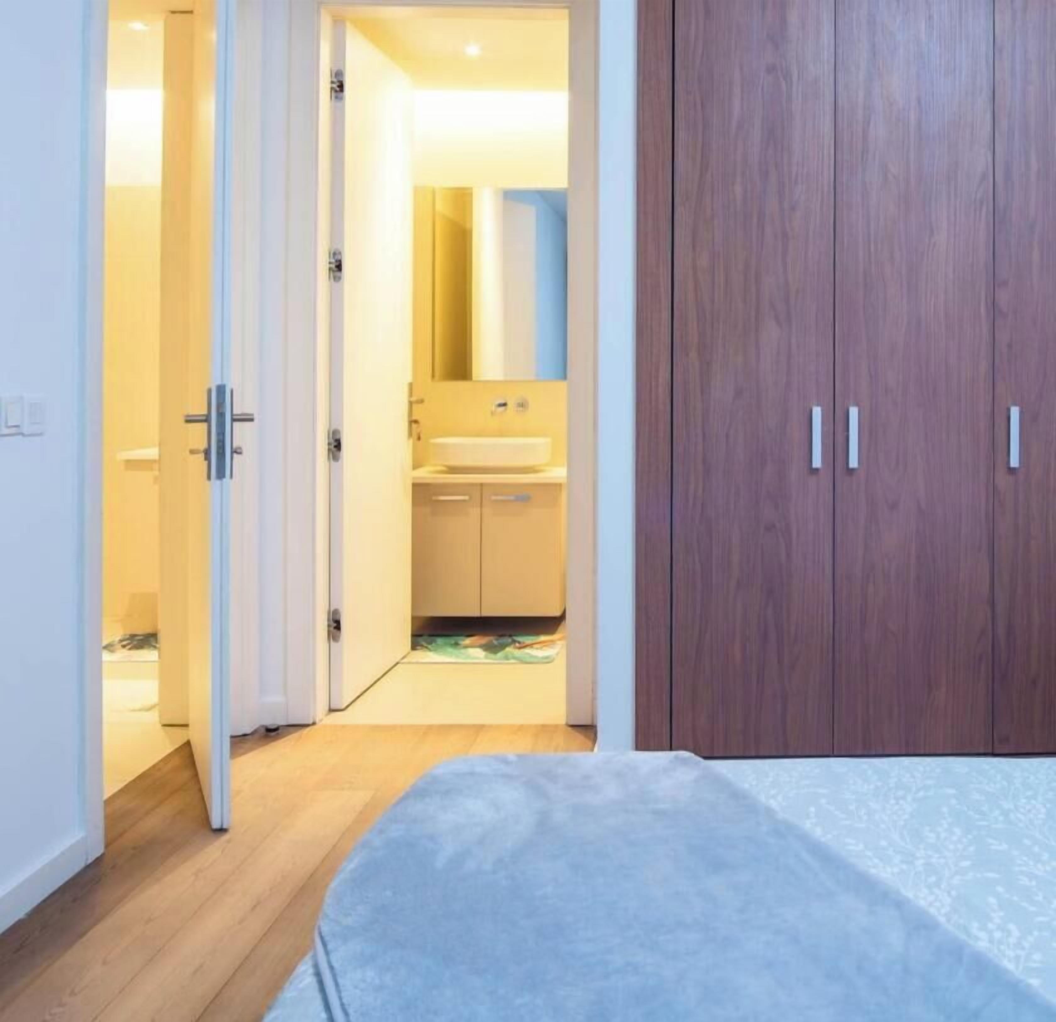 Un dormitorio con cama, armario y puerta abierta que da a un baño con lavabo y espejo.