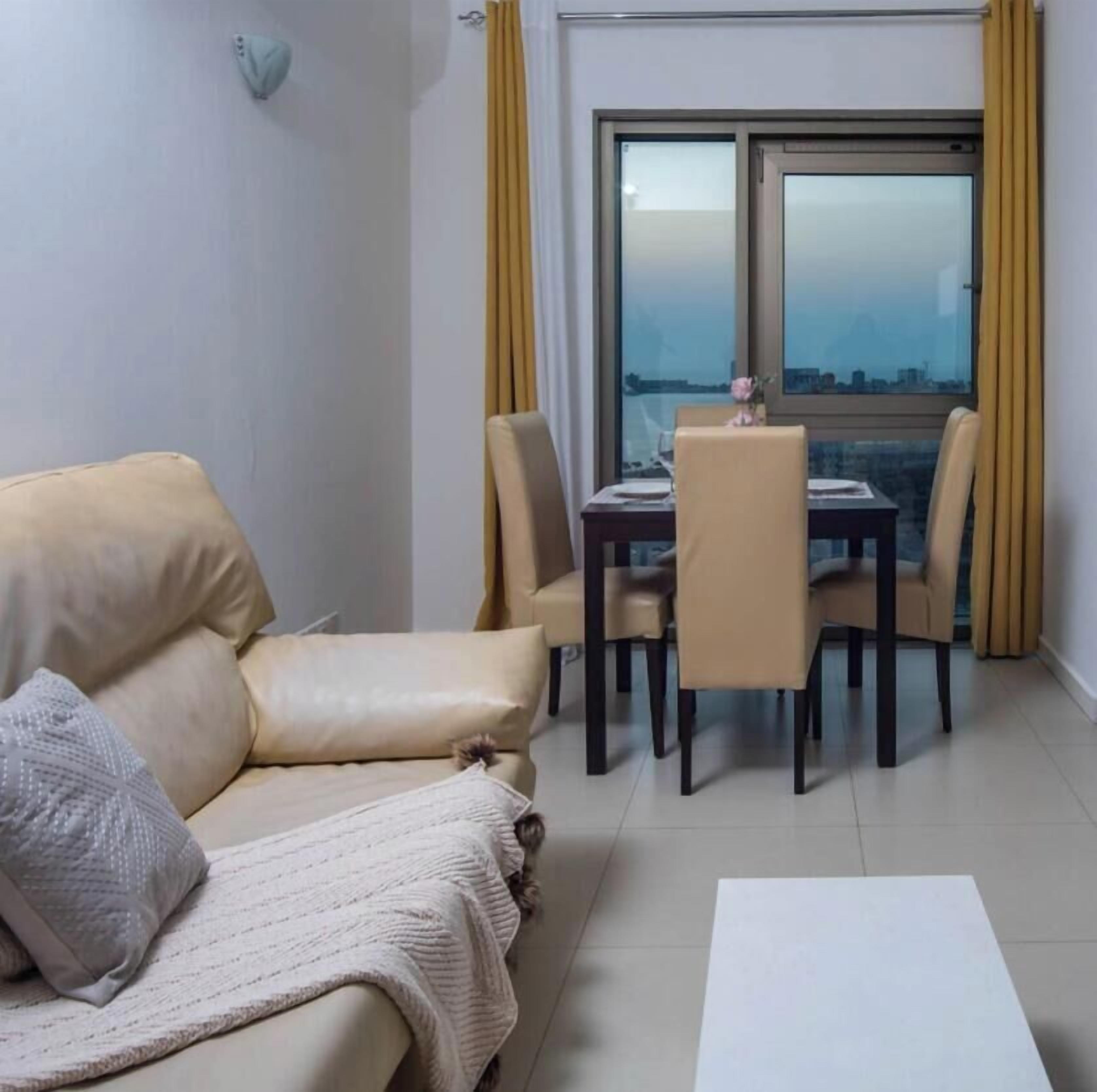 Un salon avec un canapé, une table à manger et des chaises, ainsi qu’une grande fenêtre avec des rideaux.