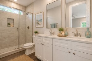 Un baño moderno con ducha envuelta en vidrio, inodoro, tocador con lavabo y un espejo grande.