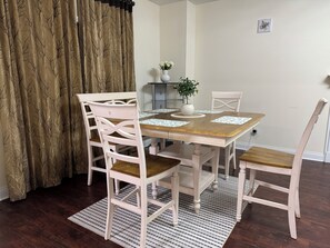 A dining area with a wooden table, white chairs, a patterned rug, and a plant on a side table. - Superb 4-bedroom house with AC  and large deck in charming Oxford,ohio (Oxford)