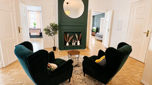 A living room with dark green armchairs, a round coffee table, and a fireplace with decorative items. - Gera Apartment Blue Foosball Table 7 Guests (Gera)