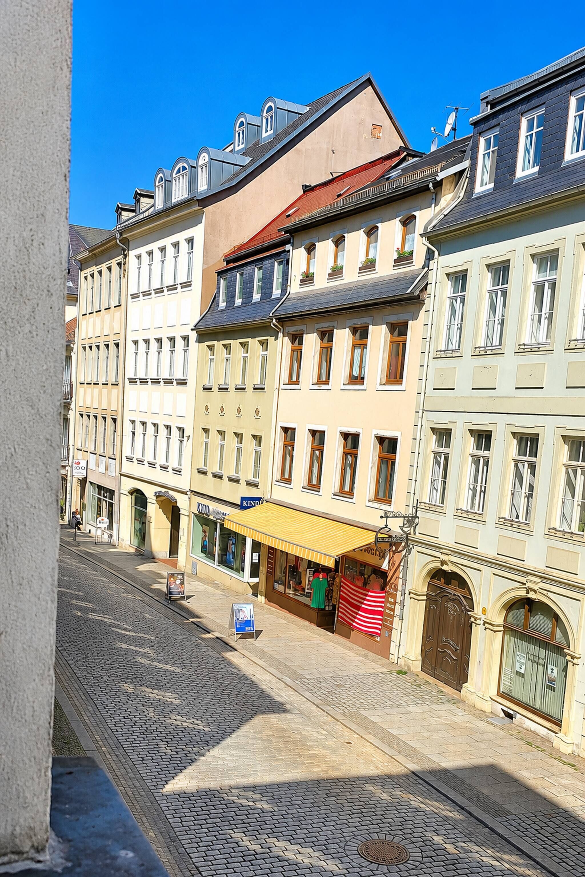 A street view with buildings, a cobblestone road, and a shop with a yellow awning.