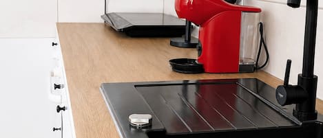 A modern kitchen with a black sink, wooden countertop, white cabinets, and a red kettle.