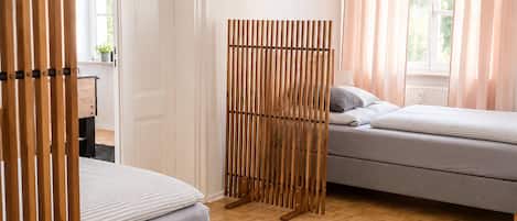 A bedroom with a bed, a sofa, a wooden partition, and a window with curtains.