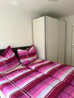 A bed with a striped bedspread and pillows, a wardrobe, and a door.