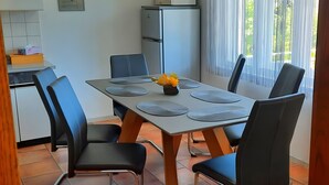 A dining area with a table set for four, surrounded by chairs, a refrigerator, and a window with curtains.
