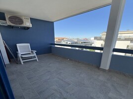 Un balcone con una sedia bianca, una ventola a soffitto e vista sugli edifici.