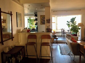 Un vaste espace de vie comprenant un coin cuisine à l’arrière, un coin repas avec des chaises et une grande plante.