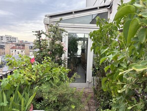 Ein Wintergarten mit Glastür zu einem Raum, umgeben von üppiger Vegetation und einer Stadtkulisse im Hintergrund.