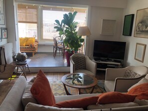 Ein Wohnzimmer mit einer Couch, Sesseln, einem Couchtisch, einem Fernseher und einem Essbereich mit Stühlen und einem Tisch.