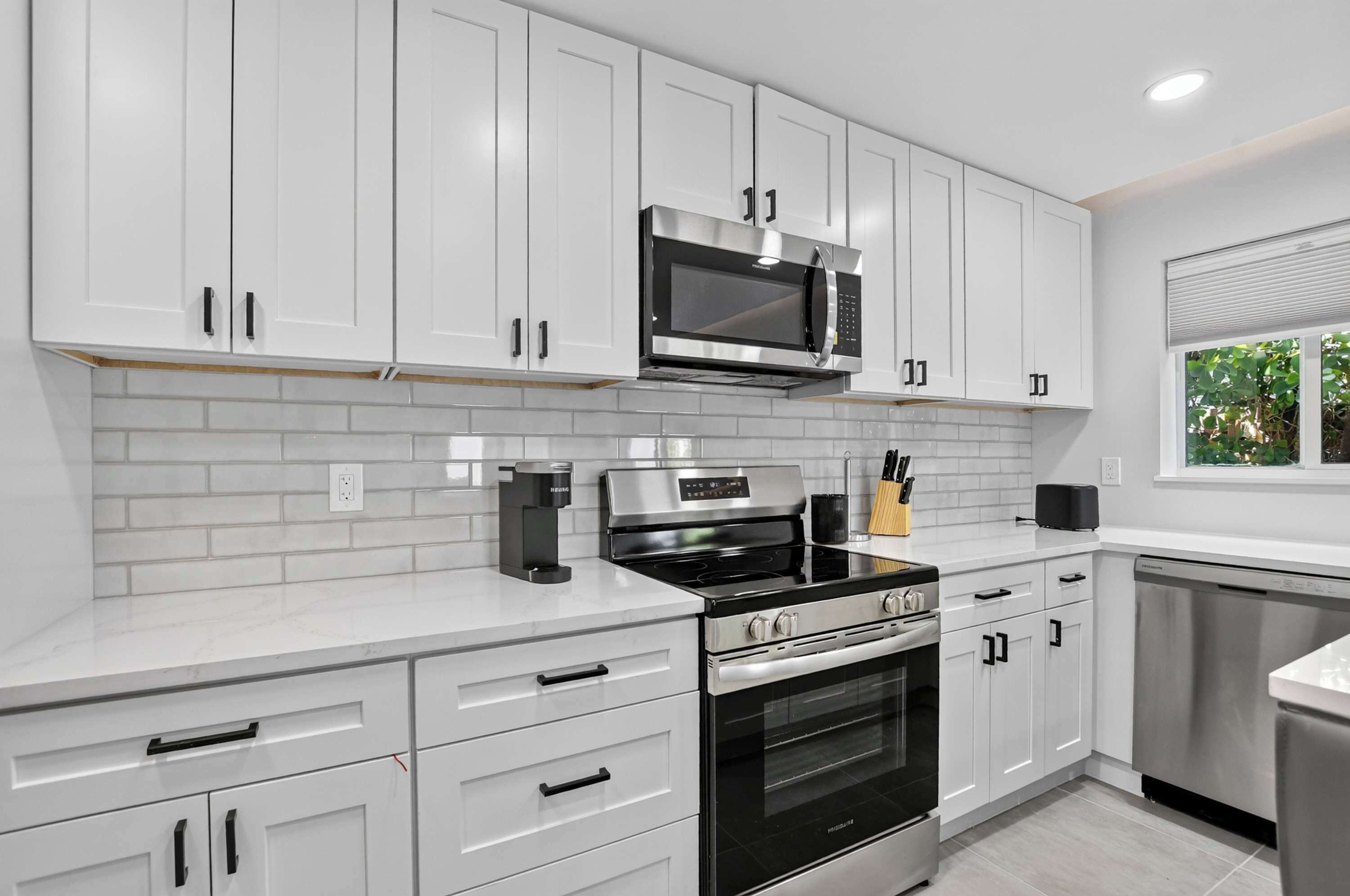A modern kitchen with white cabinetry, a stainless steel microwave, a gas stove, and a dishwasher.