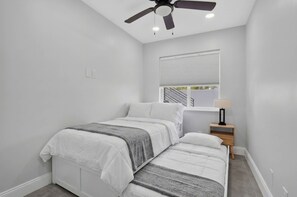 Ein Schlafzimmer mit einem Bett, einem Nachttisch, einem Deckenventilator und einem Fenster mit Jalousien.