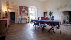 Quarto com piso de madeira, mesa de jantar com cadeiras, lareira e um quadro na parede.