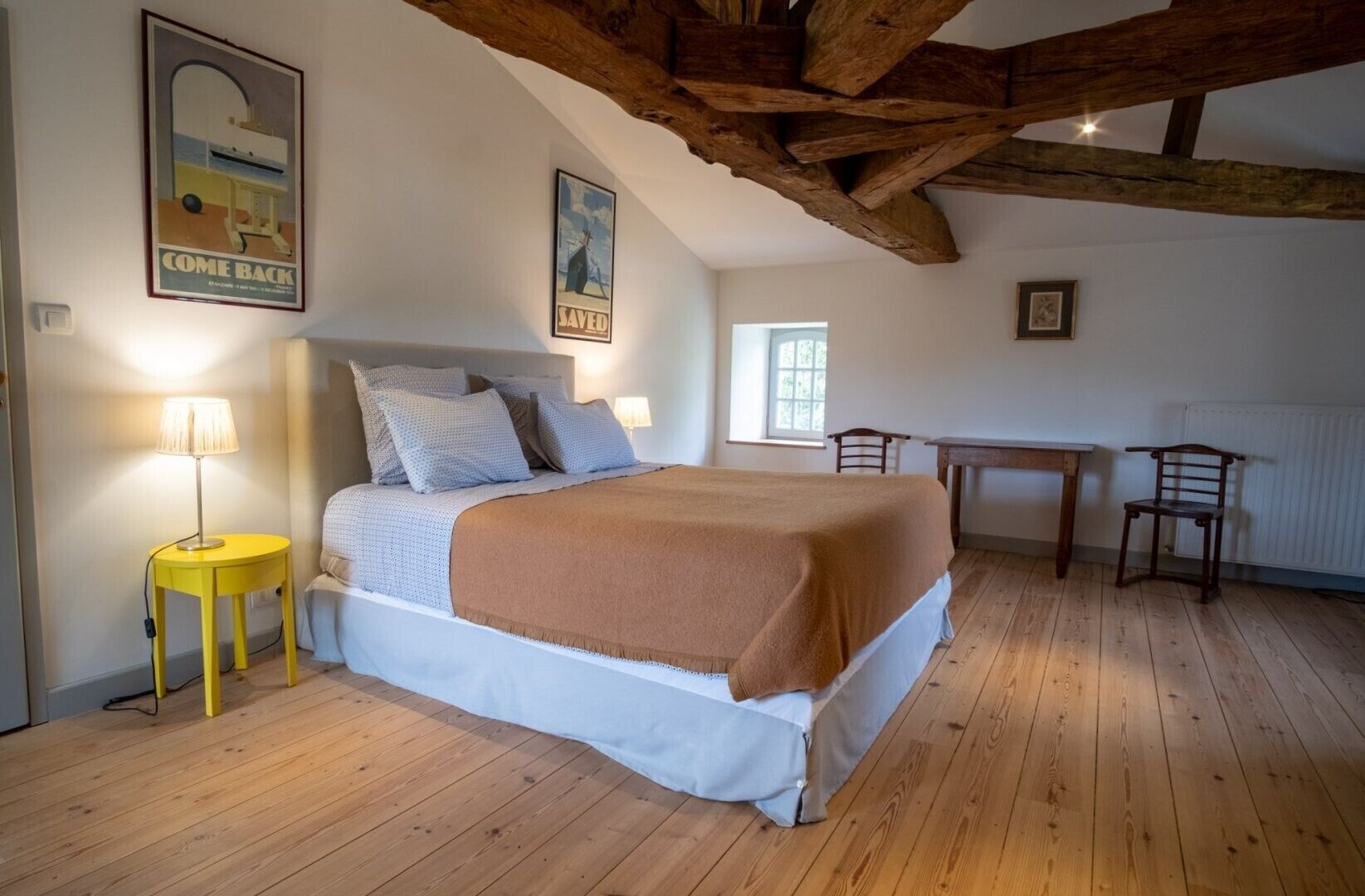 Une chambre à coucher avec un lit, une petite table, une chaise et une lampe.