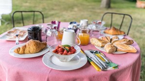 Disposição para um café da manhã ao ar livre, com croissants, morangos, suco e café sobre uma toalha de mesa rosa.