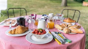 Un petit-déjeuner en plein air, avec des croissants, des fraises, du jus de fruits et du café, disposés sur une nappe rose.