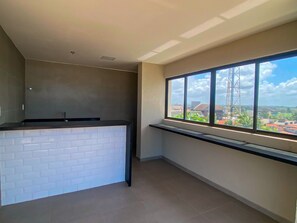 Une cuisine avec un mur recouvert de briques blanches, une fenêtre donnant sur des immeubles et une tour, et un sol carrelé.