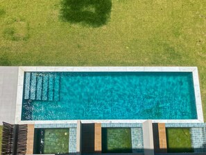Une piscine rectangulaire à l’eau d’un bleu limpide, entourée d’une terrasse carrelée et d’une pelouse.