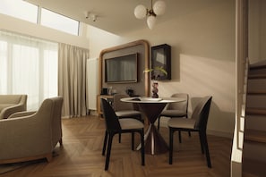 A modern hotel room with a dining area, a flat-screen TV, and a decorative vase with flowers.