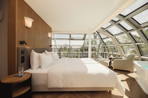 A modern bedroom with a large bed, a sitting area with a chair, and a view through a skylight.